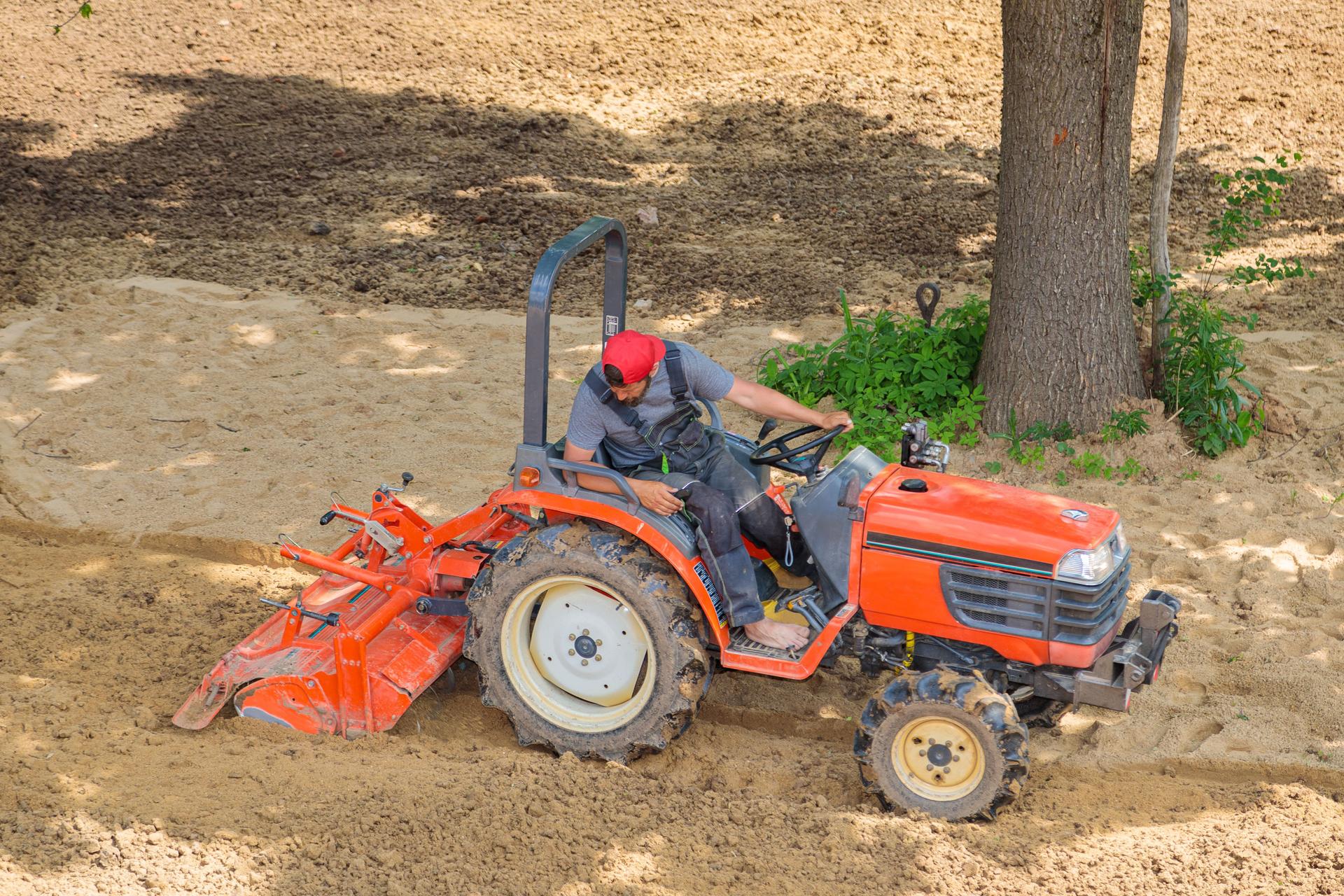 A farmer on a mini tractor loosens the soil for the lawn. Land cultivation, surface leveling